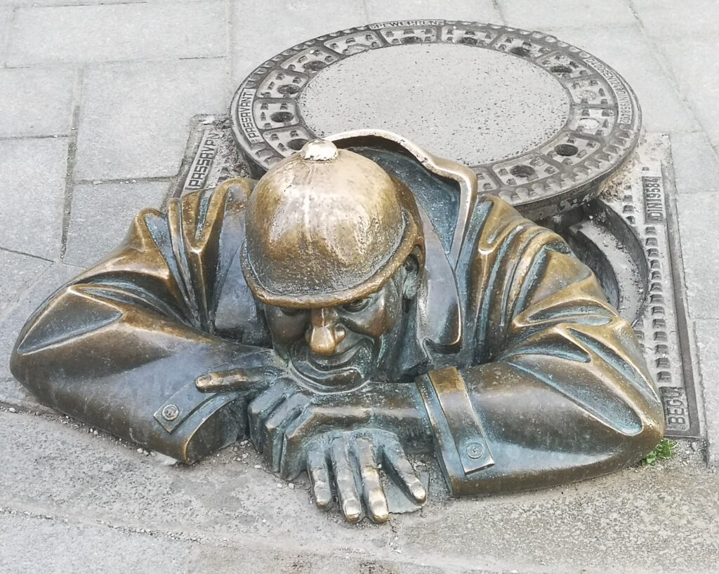 A bronze statues of a sewer worker popping up from a hole in the pavement.