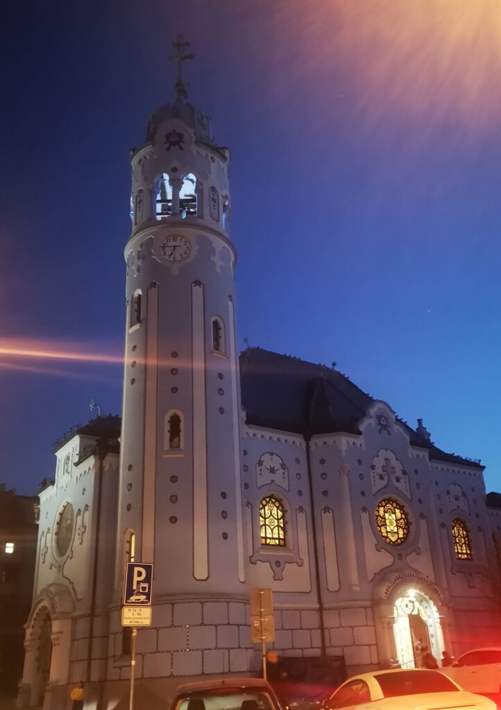 An outside view of the Blue Church and it's quirkiness. Cylindrical clock tower and stained glass windows are visible with their baby blue walls.