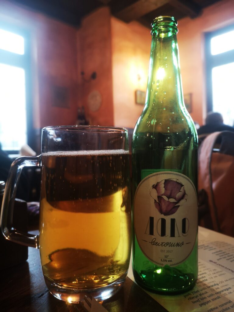 A bottle of Vitoshko Lale – Craft European Beer poured into a glass sitting next to the bottle, on a table.