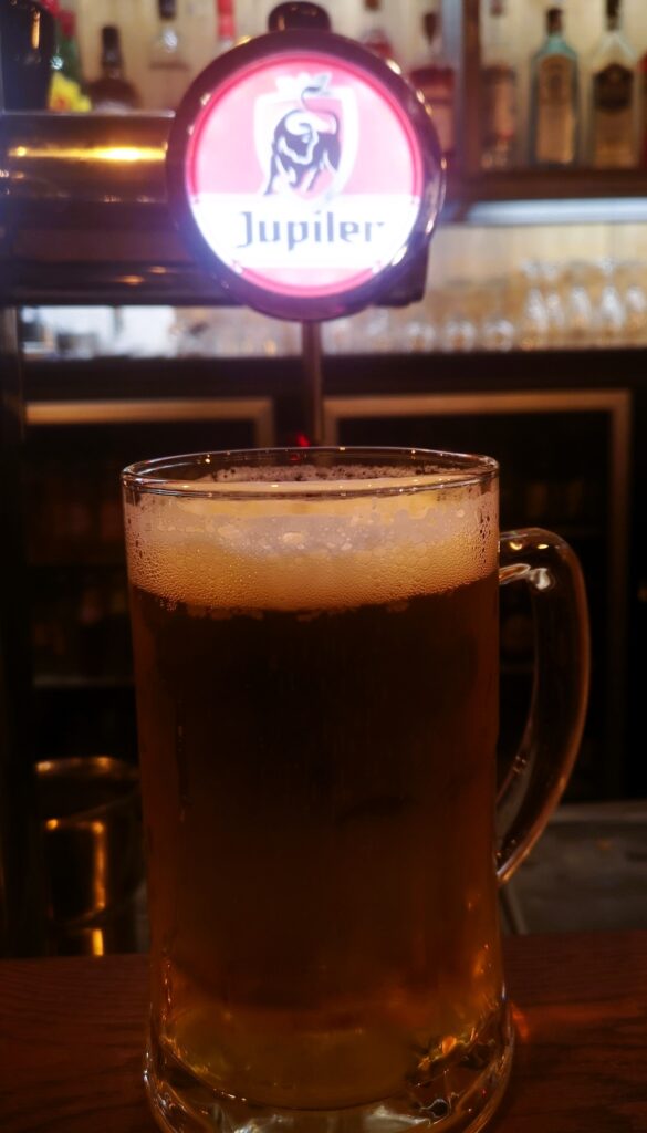 A pint of Jupiler beer on the bar in front of the beer pump in the building of Brassiere Le Louvre