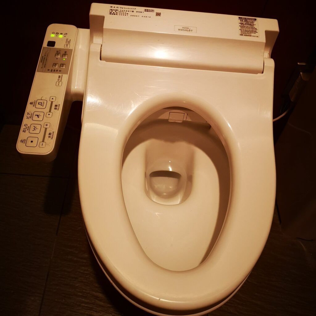 A Japanese toilet with a control panel to the left with many buttons.
