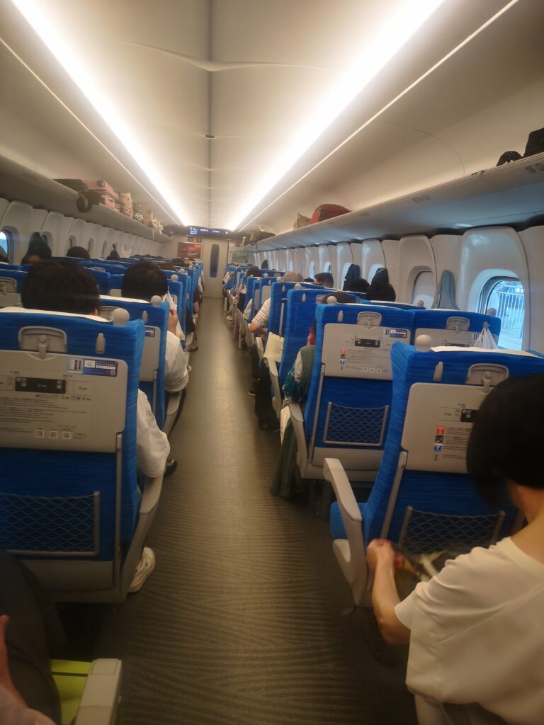 The inside of the bullet train taken from the middle of the aisleway. Rows of two-by-two seats and lining the sides of the carriage.
