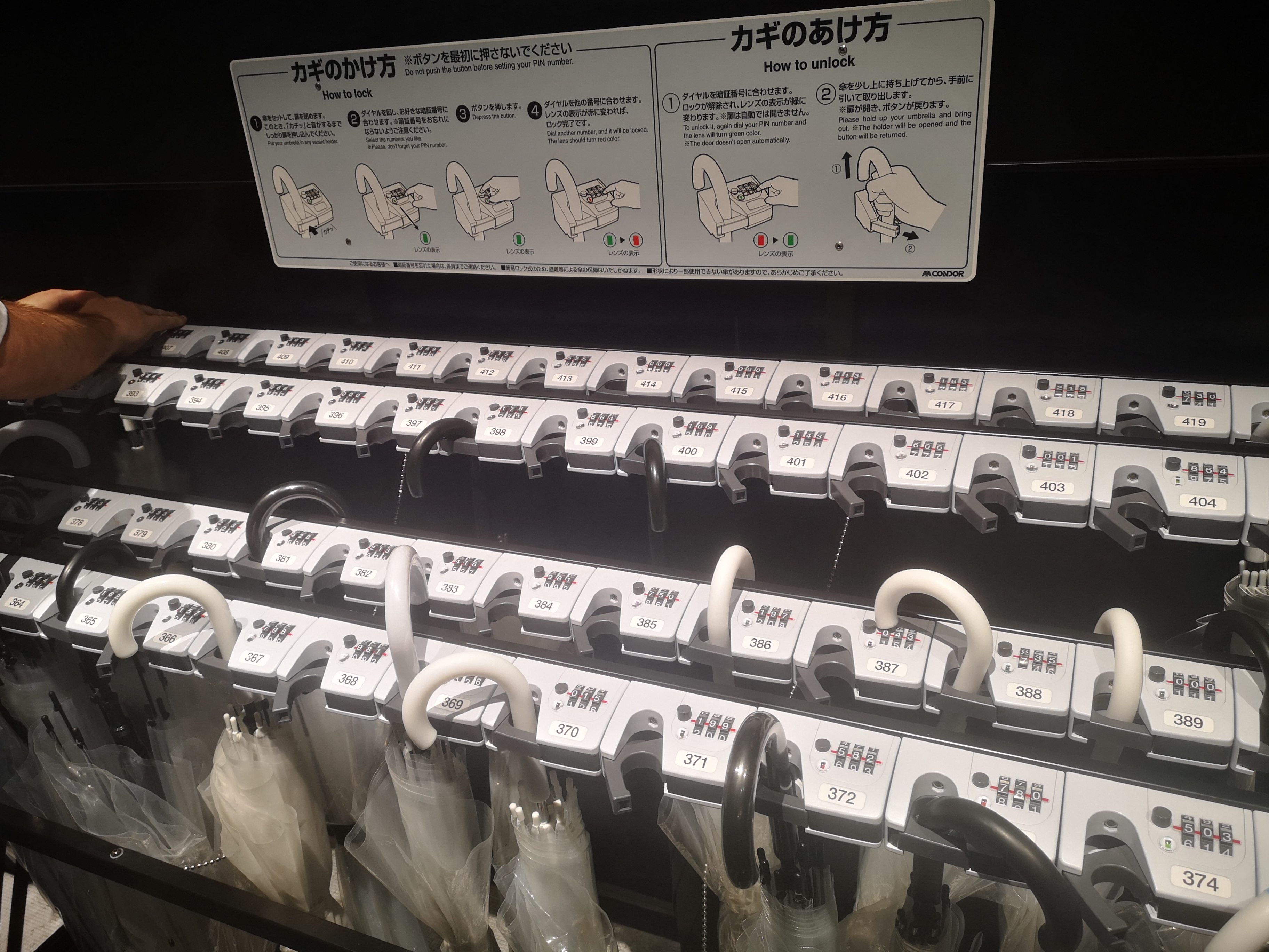 Two rows of lockable umbrella stands, complete with a smattering of umbrellas, part of the facilities at the Top Tokyo Attraction.