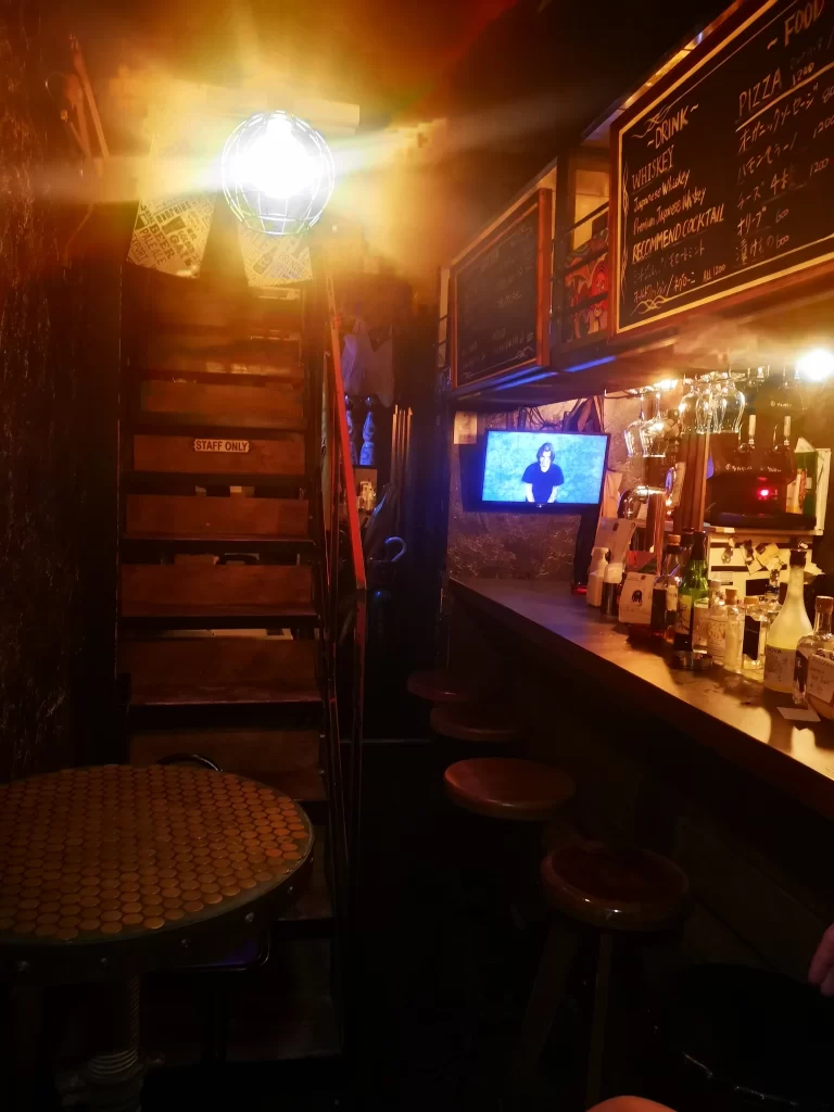 Top Tokyo Attraction, a small bar with 4 stools, a small, round table in front of a thin staircase. Less than 1.5 meters between the bar and table.